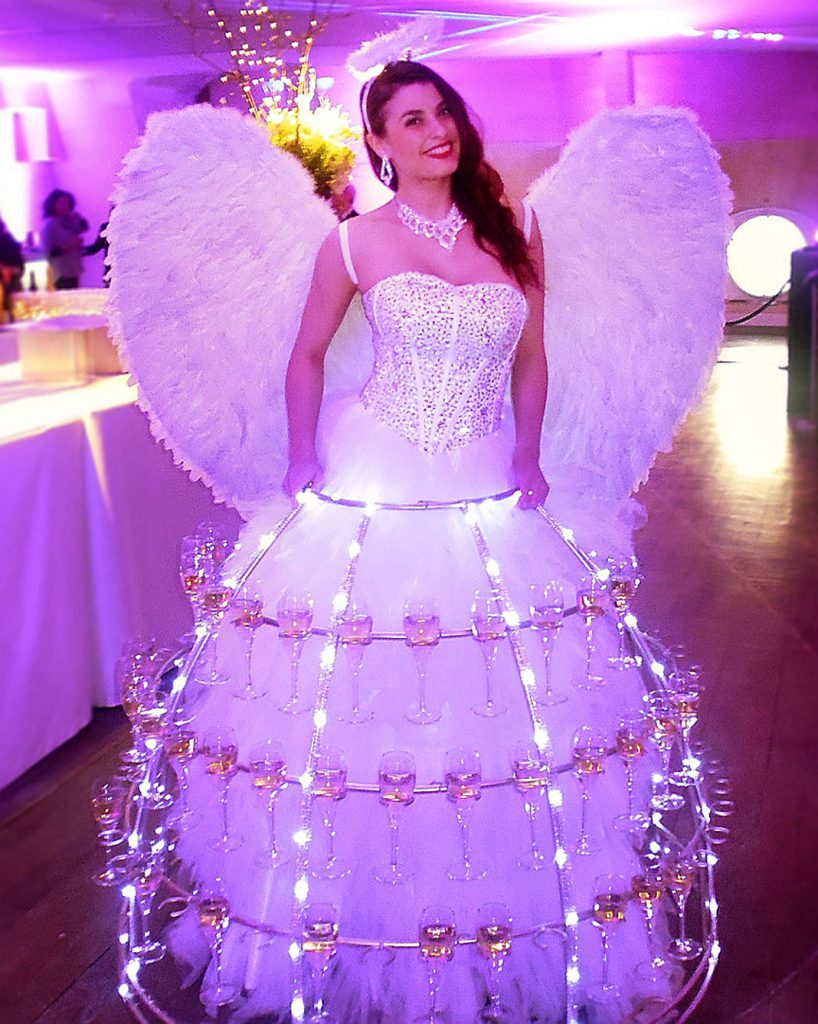 Porteuse de champagne costumée en ange lumineux avec ailes blanches